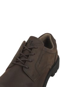 Scarpa in pelle marrone con punta tonda, logo impresso e superficie testurizzata; presenta lacci marroni e una suola in gomma nera.