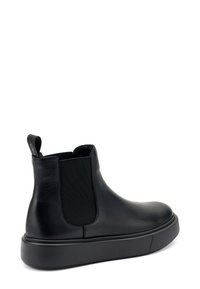 Botín negro de cuero hasta el tobillo con paneles laterales elásticos, punta redondeada y una suela gruesa de goma negra. Cuenta con una asa para ponerlo más fácilmente.