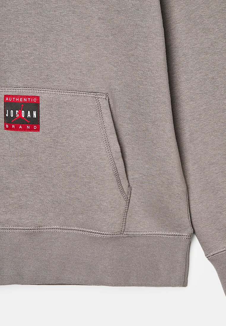 Grau Hoodie aus weichem Material mit einer Kängurutasche. Auf der Vorderseite ist ein rotes und schwarzes "Jordan Brand" Etikett zu sehen.