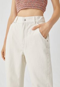 Pantalones de mezclilla beige de cintura alta, con un corte recto, bolsillos frontales y un cierre de botón plateado en la cintura.