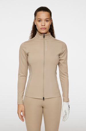 Beige langslavige zip-up shirt gemaakt van zachte stof met een opstaande kraag. Heeft een strakke pasvorm en een minimalistisch logo bij de rits.