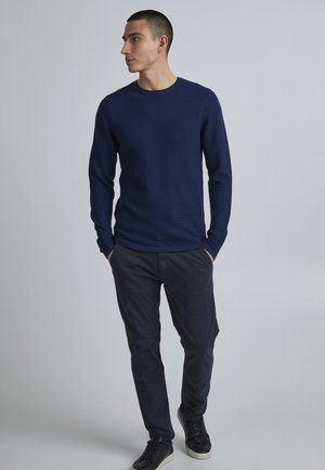 Marineblauw langemouw shirt van textuurstof, gecombineerd met donkere broeken en zwarte sneakers. Eenvoudige ronde halslijn en aansluitend ontwerp.