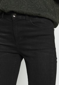 Jeans in denim neri con una forma aderente, dotati di tasca frontale, chiusura con zip e bottone metallico. Tessuto testurizzato con una leggera lucentezza.