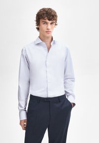 Lichtblauw overhemd met lange mouwen, een gestructureerde kraag en een gladde textuur, gecombineerd met donkere broek.