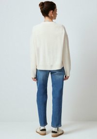 Maglione oversize color crema con orlo a coste, abbinato a jeans in denim blu dritti. Le calzature presentano accenti beige e neri con calzini bianchi.