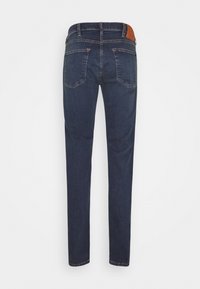 Mörkblå denimjeans sedd bakifrån med två bakfickor och en brun skinnmärkning på midjebandet.