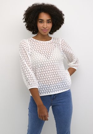 Maglione bianco in pizzo con motivo circolare, maniche a tre quarti, collo e polsini a costine, abbinato a jeans blu.