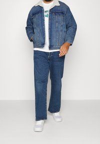 Jeansjacka med fleecemärkt krage, kombinerad med en vit t-shirt och blå jeans. Vita sneakers kompletterar outfiten.