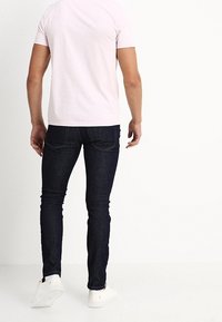 T-shirt aderente di un tenue rosa abbinato a jeans skinny blu scuro e sneakers bianche. Il tessuto appare liscio e i jeans hanno dettagli di cucitura sottili.