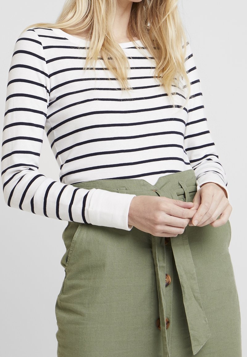 Top a maniche lunghe a righe in bianco e blu navy, abbinato a una gonna verde con cintura, caratterizzata da bottoni in legno e una finitura tessurizzata.