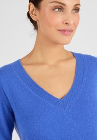 Maglione blu con scollatura a V, realizzato in morbido tessuto, caratterizzato da una texture a costine sul collo e sulle maniche. Vista ravvicinata.