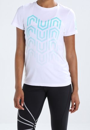 Persoon die een wit shirt met korte mouwen draagt met blauwe geometrische patronen en zwarte legging met reflecterende strepen op één been.