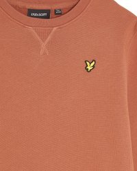 Sudadera de color óxido hecha de una tela suave. Presenta una costura en V en el cuello y un logo de un pájaro amarillo en el pecho.