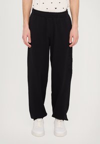 Black sweatpants with an elastic waistband, loose fit, and side cargo pocket detailing. Material appears soft and textured.