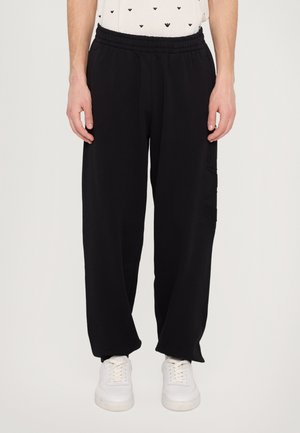 Black sweatpants with an elastic waistband, loose fit, and side cargo pocket detailing. Material appears soft and textured.