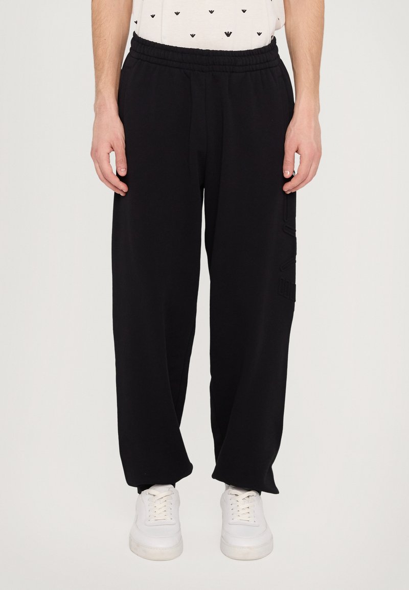 Black sweatpants with an elastic waistband, loose fit, and side cargo pocket detailing. Material appears soft and textured.