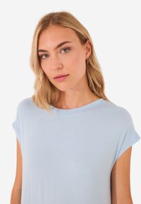 T-shirt azzurro di cotone a maniche corte, realizzato in tessuto morbido. Presenta un colletto a girocollo e decorazioni sottili sulla parte anteriore.
