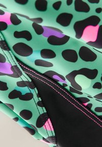 Zielona tkanina w czarną, różową i fioletową wzór lamparta. Charakteryzuje się kontrastowym czarnym przeszyciem wzdłuż szwu, gładką teksturą.