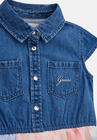 Farmer ing, galléros nyakkal, két mellzsebbel, ezüst patent gombokkal és hímzett logóval. Az alsó része pasztell ombre fodorral díszített.