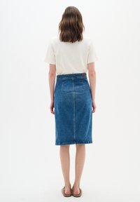 Fustă tip creion din denim de culoare albastru mediu, cu fanta la spate, material texturat și talie înaltă cu cusături vizibile.