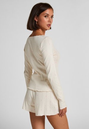 Roomkleurige top met lange mouwen en bijpassende shorts met roze hartjespatronen. Geribbelde textuur en aflopende randen. Lichtgewicht stof.