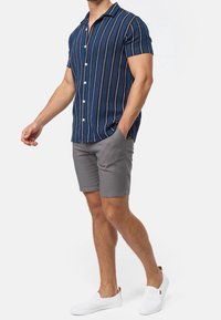 Koszula z krótkim rękawem w kolorze granatowym z białymi pionowymi paskami, zestawiona z szarymi szortami. Białe buty wsuwane. Casualowy, lekki materiał.