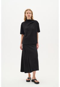 Čierny, oversized top s vysokým golierom skombinovaný s prislúchajúcou obalovou sukňou. Oblečenie je vyrobené z hladkej látky so jednoduchým dizajnom.