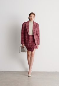 Rose-check patterned blazer and skirt set in textured fabric, paired with a beige turtleneck and light gray handbag. White heels.