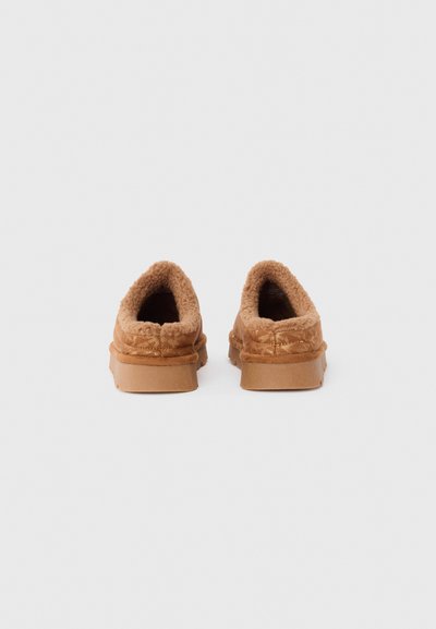 Bruna slip-on skor med mjuk foder, rundad baksida och texturerad yta. Gummisulor syns, med minimalt dekorativt sömnadsdetaljer.