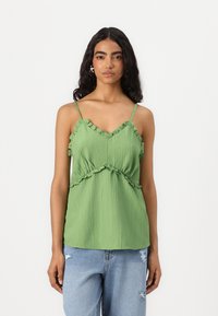 Grønn plisserte topp med volanger på stroppene og nederkanten, med en tettsittende bodice og løs nederdel, kombinert med slitte blå jeans.