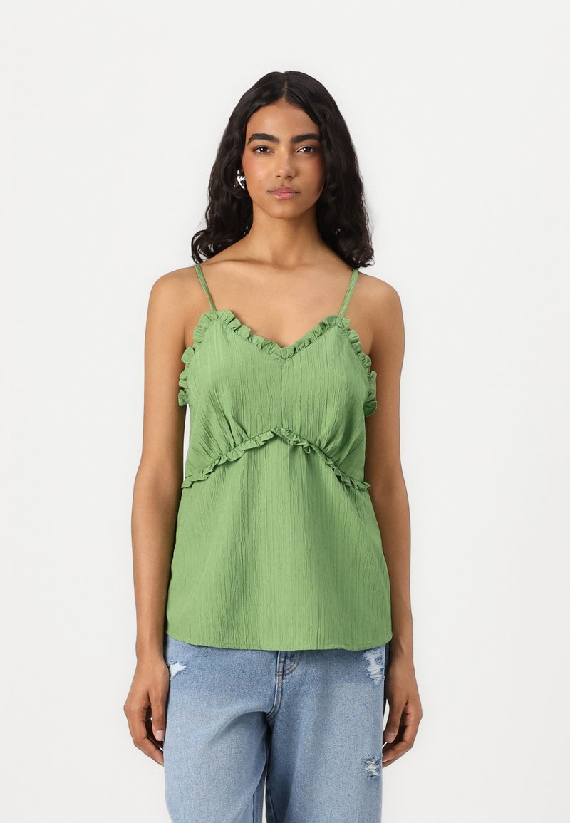 Grønn plisserte topp med volanger på stroppene og nederkanten, med en tettsittende bodice og løs nederdel, kombinert med slitte blå jeans.