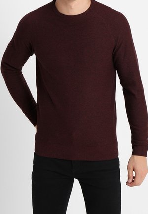 Burgundy tröja gjord av stickat tyg, med rund hals, långa ärmar och ribbade muddar och fåll. Buren med svarta byxor.