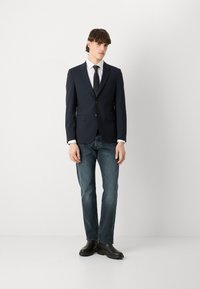 Tumesinine bleiser, millel on sooniklapid, kaks esikot, koos valge särgi ja musta lipsuga, helesinised teksad ning mustad ankle saapad.