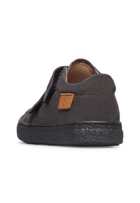 Zapatillas de ante gris oscuro con una superficie texturizada, suela de goma negra plana y un parche de cuero marrón en la parte trasera. Cierre de velcro.