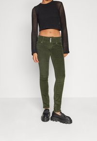 Zelené kordové kalhoty slim fit, vybavené třemi předními knoflíky a bočními kapsami, v kombinaci s černým krátkým pleteným topem.