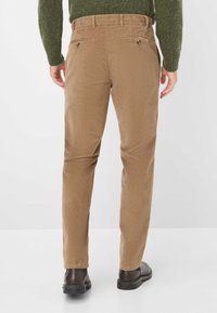 Pantaloni in corduroy marroni con un design a gamba dritta, dotati di tasche posteriori e chiusure a bottone, abbinati a scarpe scure e a un maglione verde.