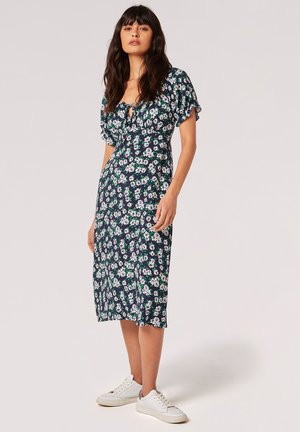 Blumen-Midi-Kleid in Marineblau mit weißen und grünen Gänseblümchen, ausgestattet mit Puffärmeln, einem Bindeband vorne und kombiniert mit weißen Sneakern.