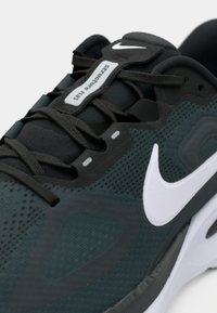 Chaussure de course Nike en mesh vert foncé, avec un logo swoosh blanc, des accents gris et des détails texturés sur la tige et la semelle.