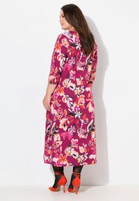 Vestido maxi floral en tonos rosas, rojos y negros. Presenta mangas de tres cuartos y un vibrante patrón de flores. Combinado con tacones naranjas.