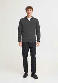 Suéter de punto gris con cuello en V, mangas largas y puños acanalados, combinado con pantalones negros y zapatos negros. Textura suave y corte relajado.
