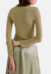 Maglione in verde oliva, con maniche lunghe e un design testurizzato, abbinato a una gonna di una leggera tonalità verde seta.
