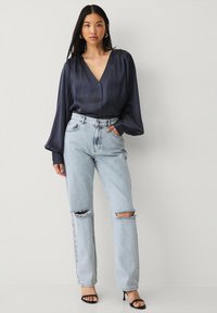 Mørkeblå satinbluse med frontknapper og pufærmer, parret med lyseblå ripped straight-leg jeans og sorte hælede sandaler.