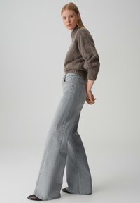 Jeans larghi grigi in denim, abbinati a un maglione marrone in knit morbido. I jeans presentano una vita alta e tasche sottili.