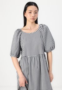 Vestido de gingham preto e branco com mangas bufantes, decote redondo e saia em camadas. Feito de um tecido leve com uma textura suave.