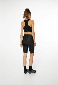 Crni sportski crop top i biciklističke kratke hlače, sa uskim dizajnom, teksturiranim panelima i glatkim završetkom. Crne sportske cipele upotpunjuju izgled.