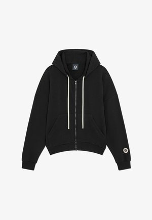 Sudadera negra con cremallera, bolsillos delanteros, cordones blancos, puños acanalados y un parche circular con logo en la manga izquierda.