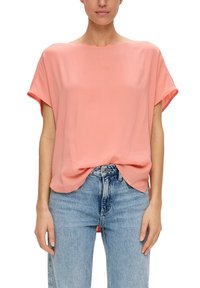 Rosa, kurzärmelige Bluse aus leichtem Stoff mit lockerer Passform und abgerundetem Saum. Kombiniert mit hellblauen Jeans.