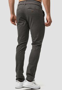Pantalones gris con patrón de corte slim, bolsillos traseros y una cinturilla texturizada, combinados con zapatillas blancas.