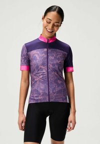 Maillot de cyclisme à manches courtes en violet avec un motif floral, doté d'un col et d'une fermeture éclair roses. Associé à un short de cyclisme noir.