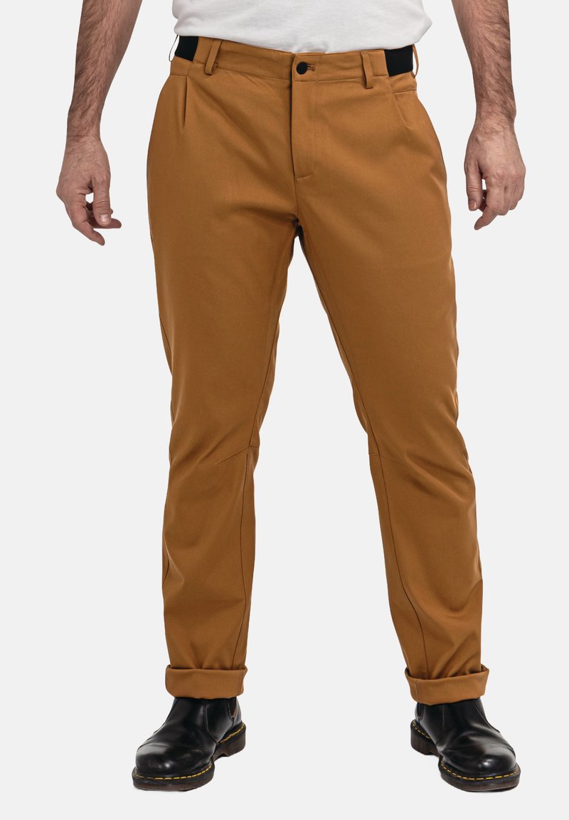 Beige Hosen mit taillierter Passform, ausgestattet mit einem Reißverschluss, Vordertaschen und sichtbaren Nähten, kombiniert mit schwarzen Stiefeln.